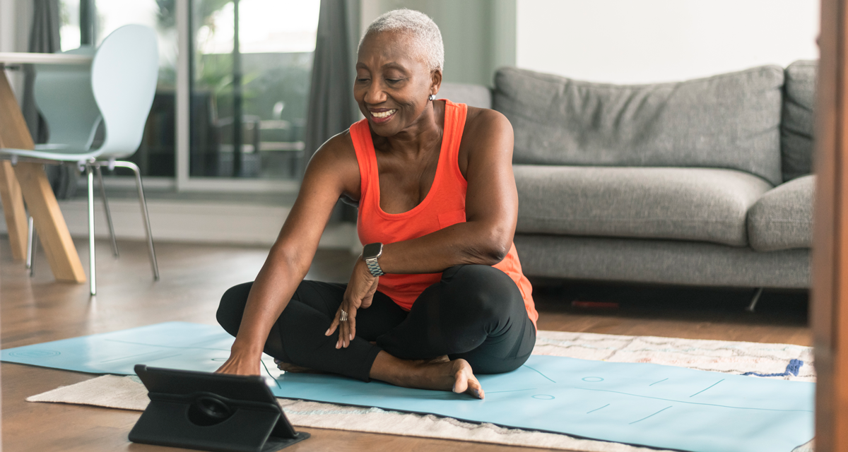 mature woman sitting on yoga mat touching tablet to exercise